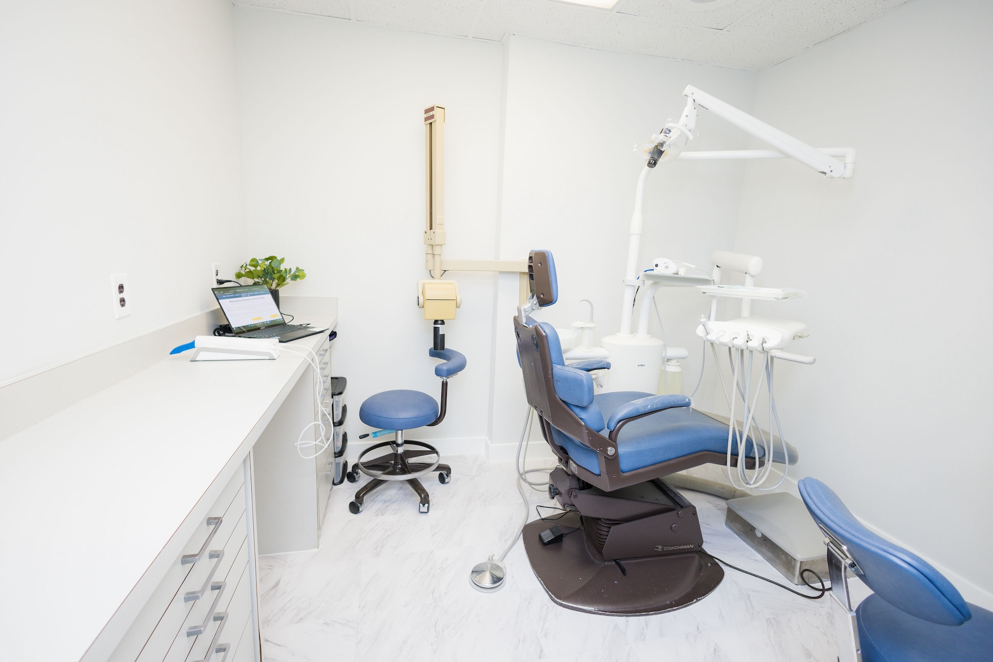 An image of a dental office interior, featuring dental chairs, equipment, and a reception area with a desk and computer monitor.