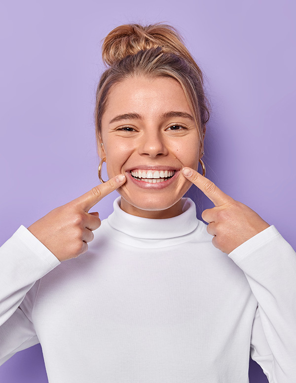 Woman with a big smile, holding her teeth together with her index finger and thumb.