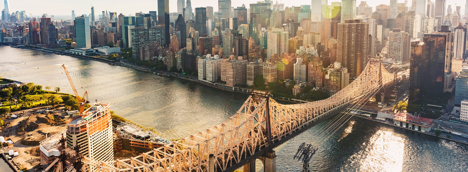 Aerial view of a city skyline with the Brooklyn Bridge, Manhattan skyscrapers, and the Hudson River in the foreground.