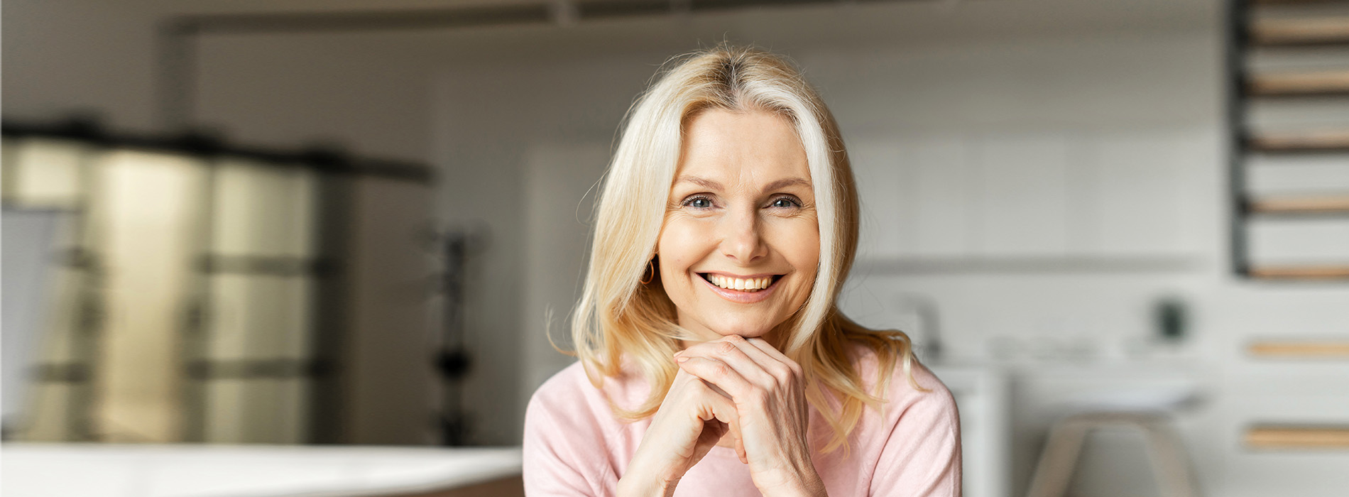 A woman is standing in a kitchen, smiling at the camera.