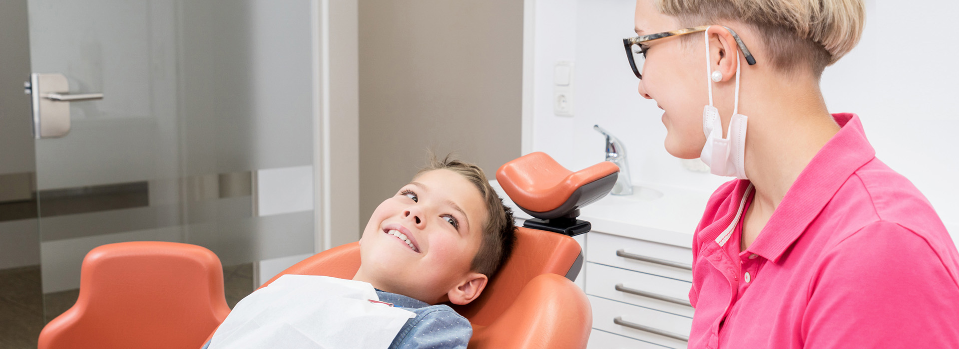 A child in a dental chair receiving treatment with a dentist and dental hygienist present.