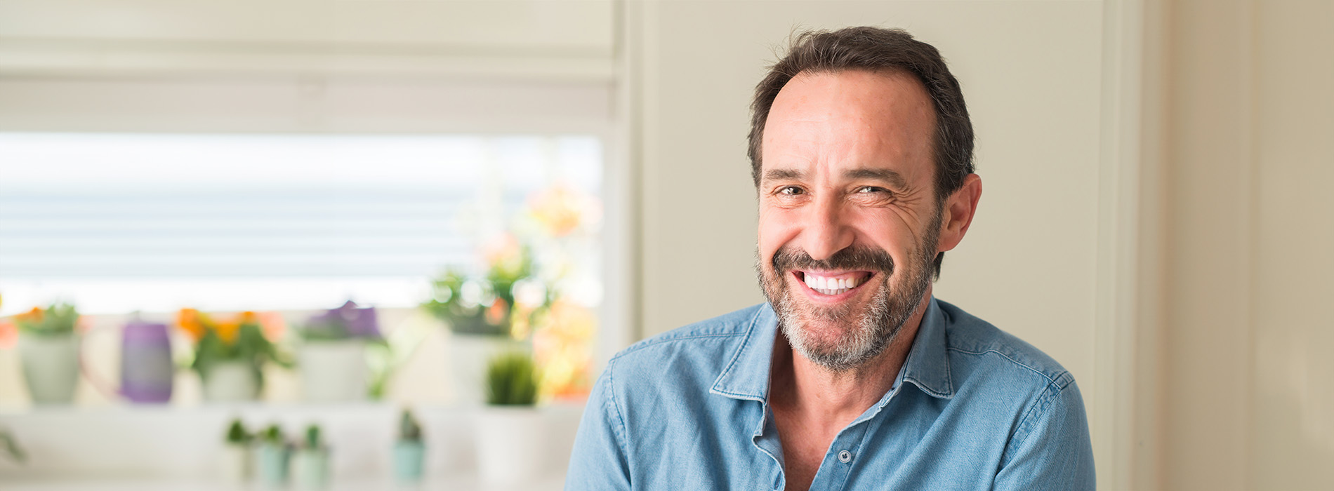 The image shows a man sitting at a table, smiling and looking directly into the camera.