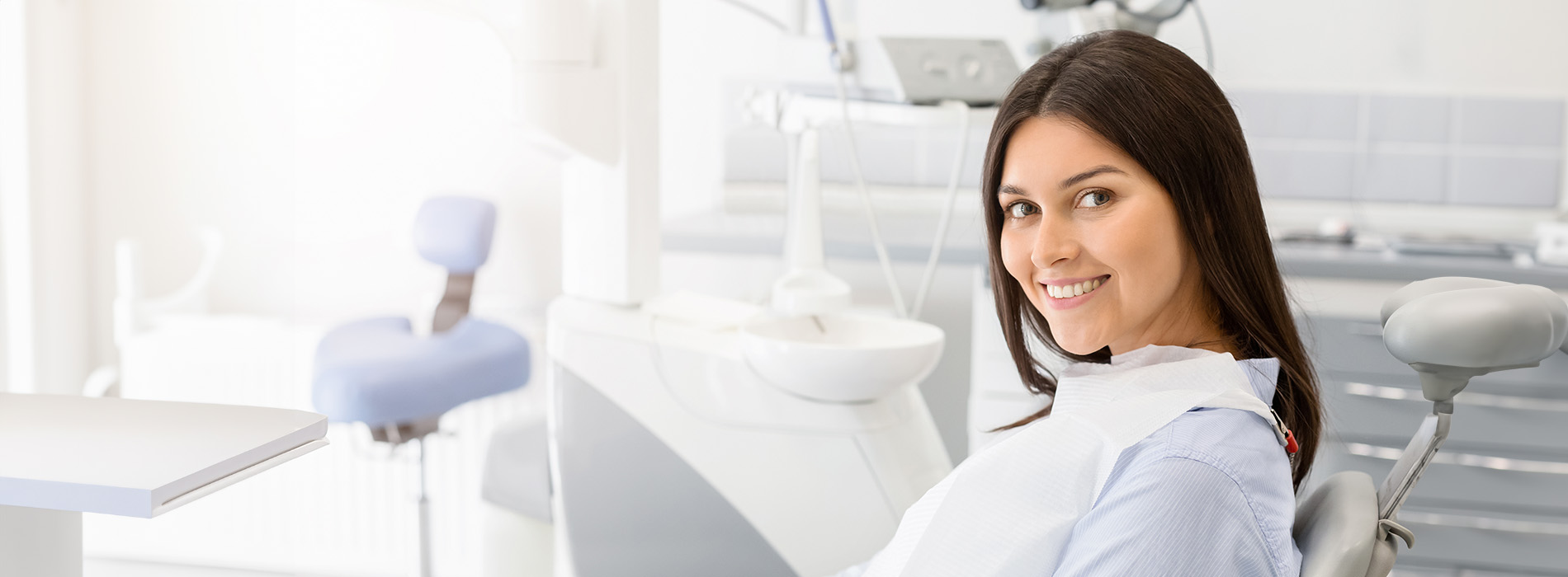 A woman sitting in a dental chair, smiling at the camera, with her mouth open as if she is speaking or being examined.