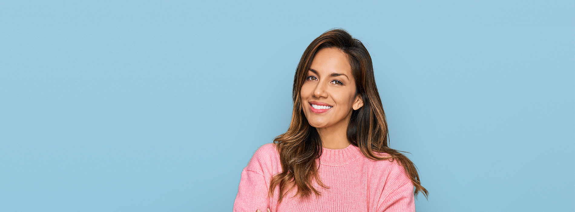 The image shows a woman with a smile, standing against a blue background. She has dark hair and is wearing a pink top.