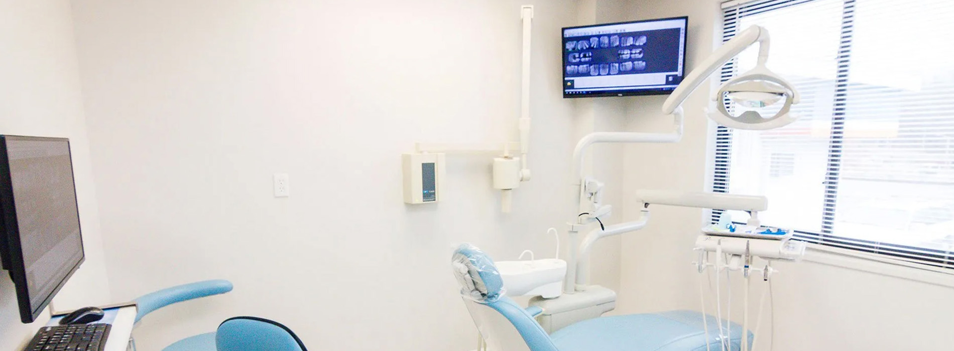 The image shows an interior view of a dental office with equipment, including a dental chair and a monitor displaying medical images.