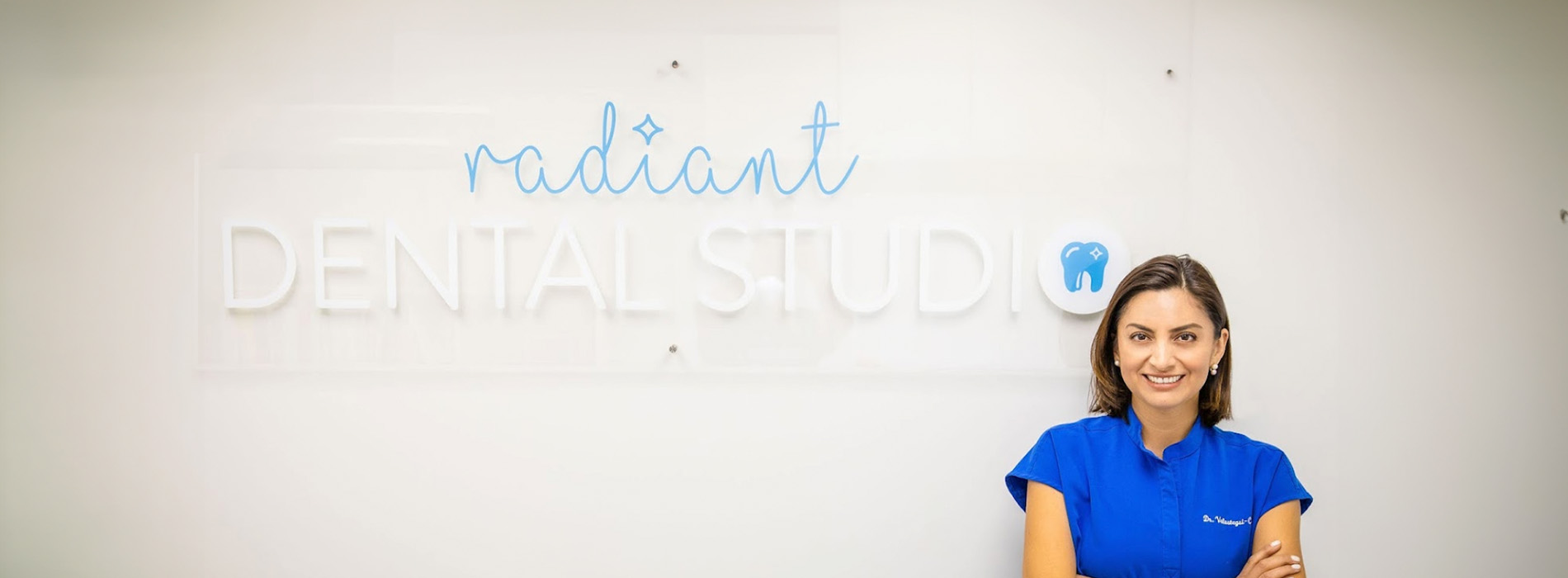 A person standing in front of a whiteboard with the text  Radiant Dental Studio  and a logo for dental services, smiling at the camera.