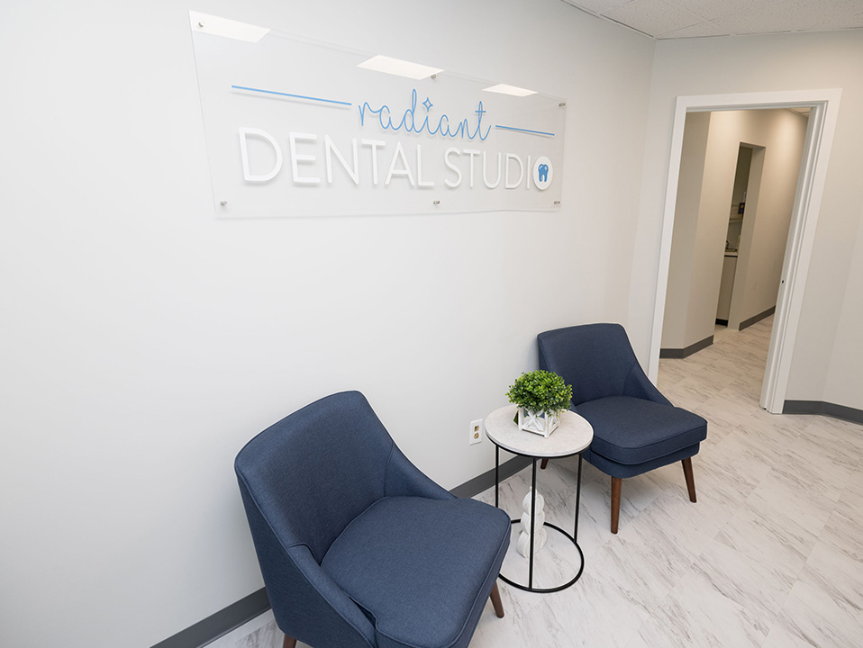 An interior view of a dental studio s waiting area, featuring a modern design with a blue couch, a coffee table, and a potted plant.