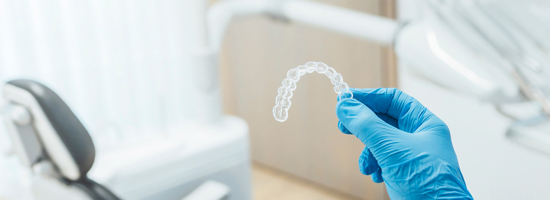 A medical worker wearing blue gloves is holding a transparent, melted plastic item in front of a dental chair.