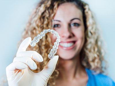 The image shows a person holding up a clear, plastic dental retainer with their hands.