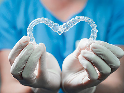 The image features a person wearing medical gloves and holding a clear plastic object that resembles a heart, with the background out of focus.