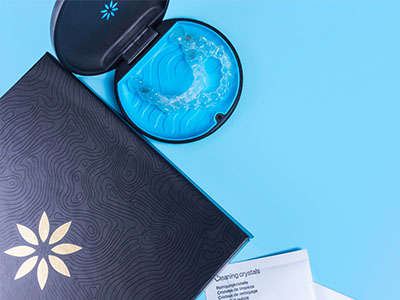 A blue toothbrush with a clear bristle head in its package, placed next to an open book with a floral pattern on a light blue background.