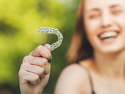 A smiling woman holding a clear, plastic dental retainer with a playful expression.