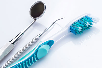 The image shows a collection of dental instruments, including a toothbrush with blue bristles and a metal dental mirror, laid out against a white background.