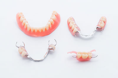 A photograph of three pairs of dentures with a focus on the upper front teeth, showcasing different styles and tooth colors against a white background.