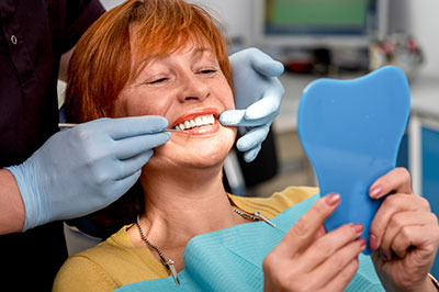 A woman in a dental chair receiving a teeth cleaning, with a dentist and hygienist attending to her.