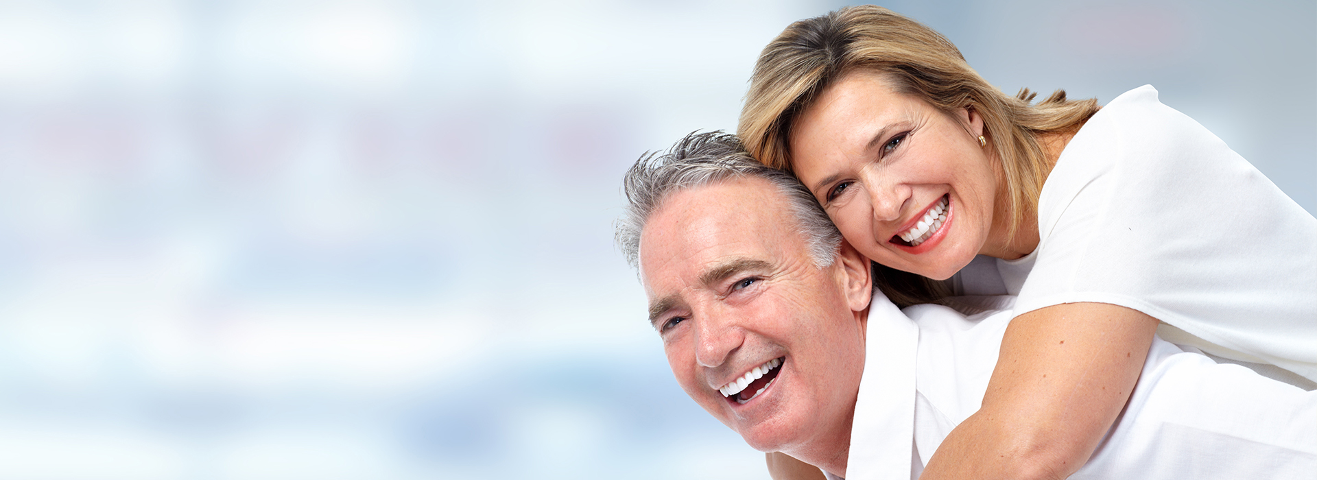 An elderly couple sharing a joyful moment together, with the man in a white shirt and the woman in a light-colored blouse.