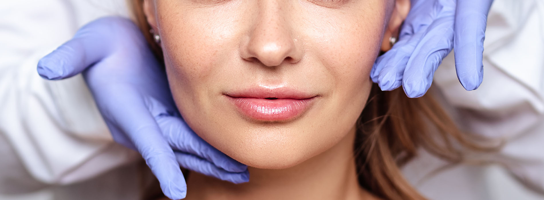 A woman with a mask over her face is having her makeup done by someone wearing blue gloves.