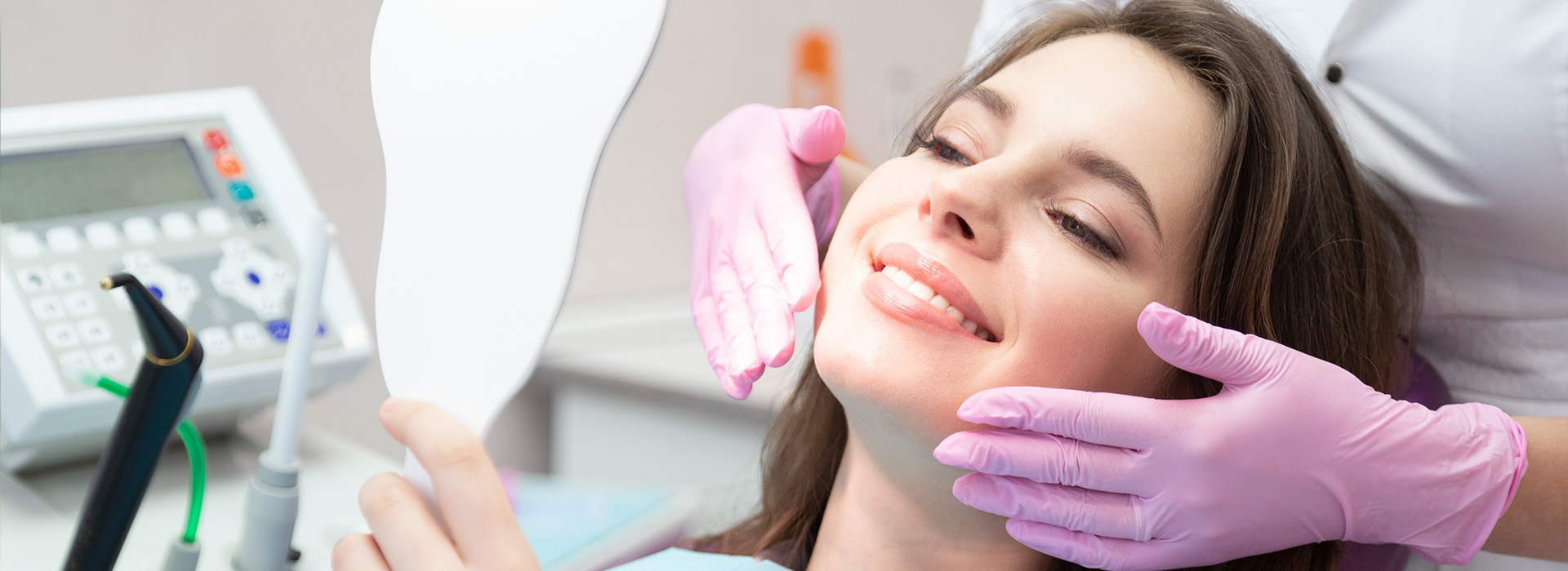 A woman is seated in a dental chair, receiving dental care with a smile on her face.