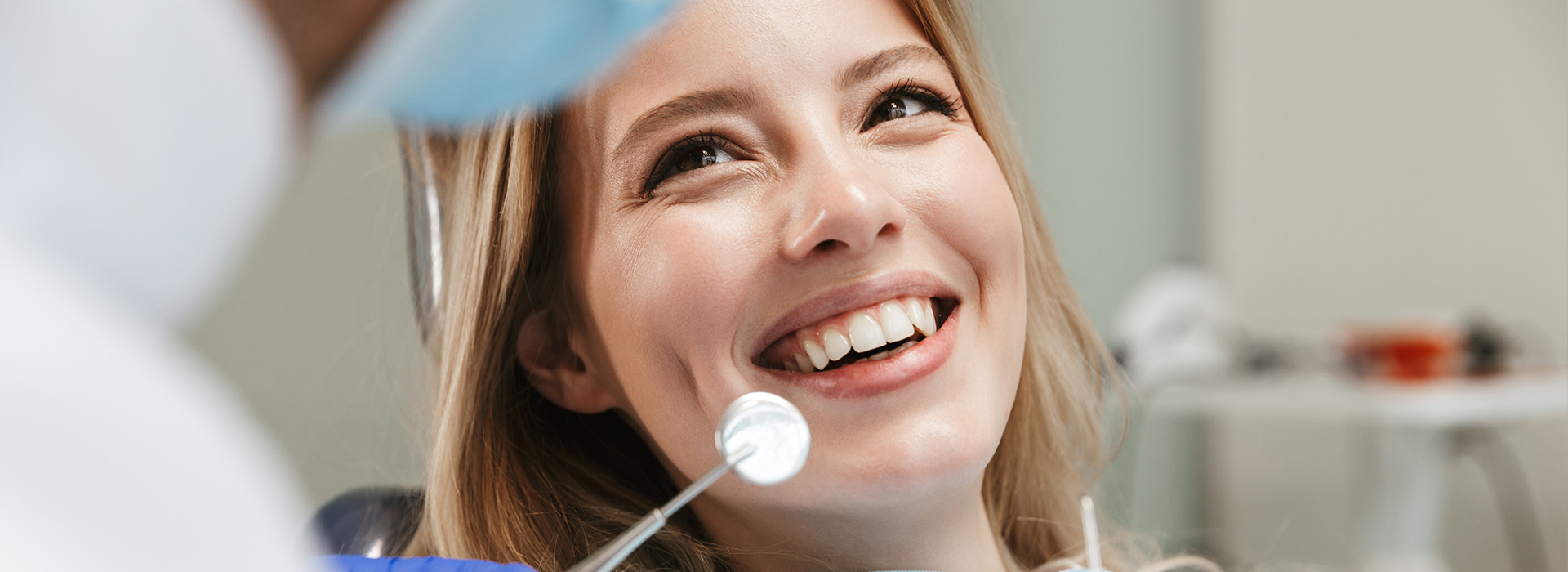 A woman in a dental chair, smiling at the camera, with a dental professional standing behind her.