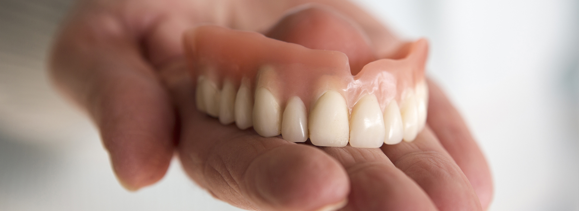 A person s hand holding a denture set with artificial teeth.