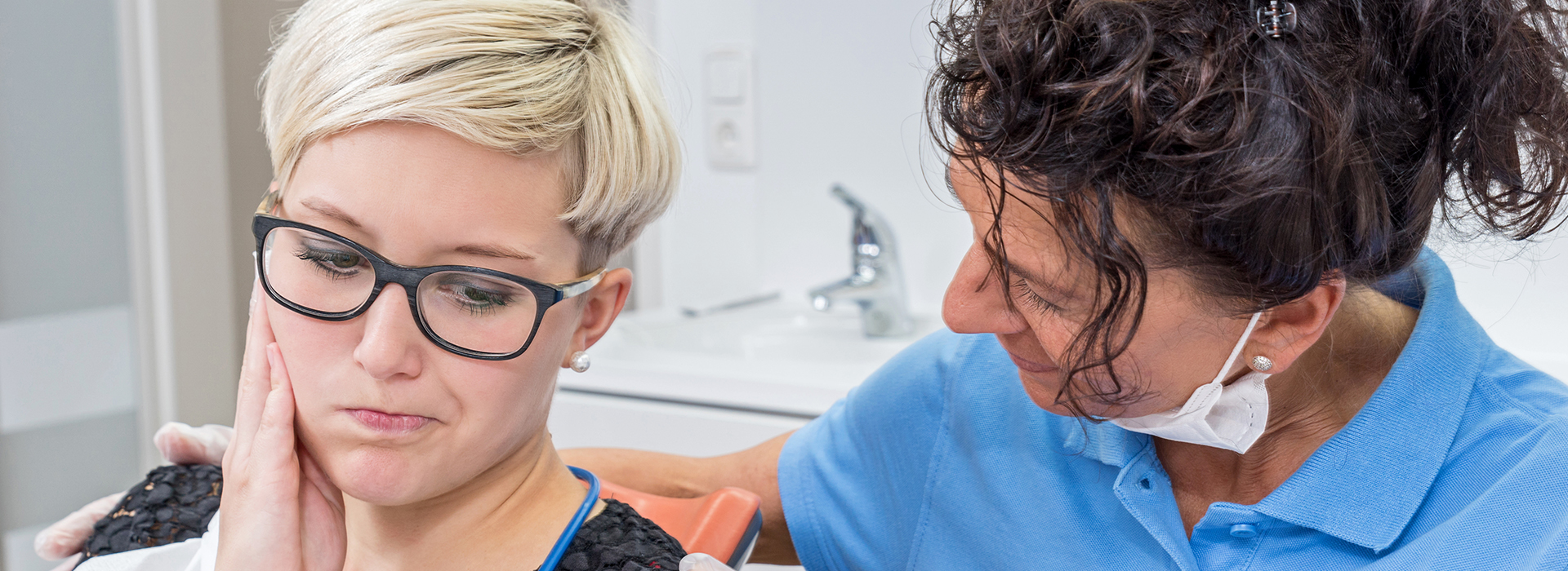 The image shows a woman with glasses receiving dental care from a professional, likely in a dental office setting.