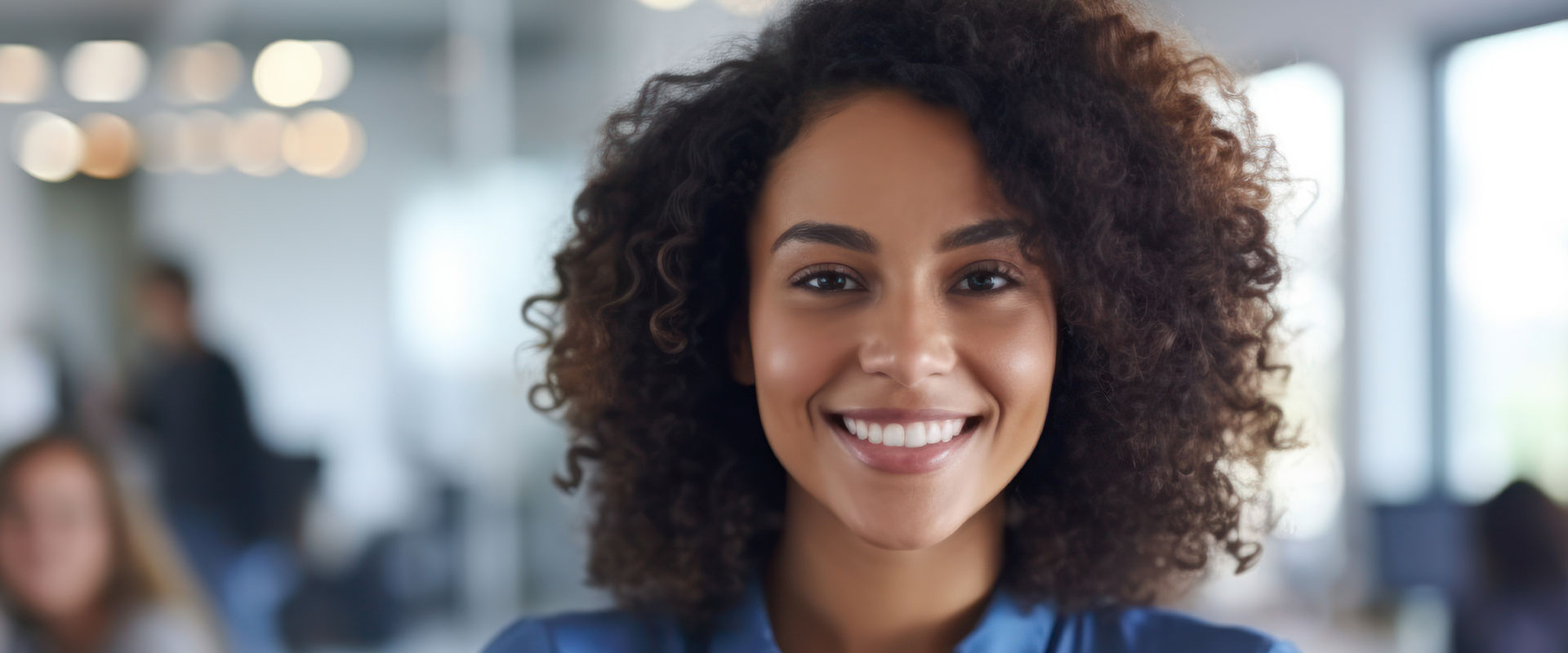 A woman with curly hair, smiling at the camera, in a professional office setting.