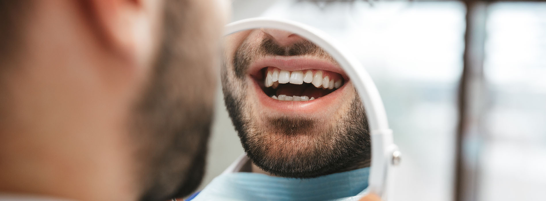 A man with a beard in a dental office, smiling and holding his mouth open while sitting in the dentist s chair.