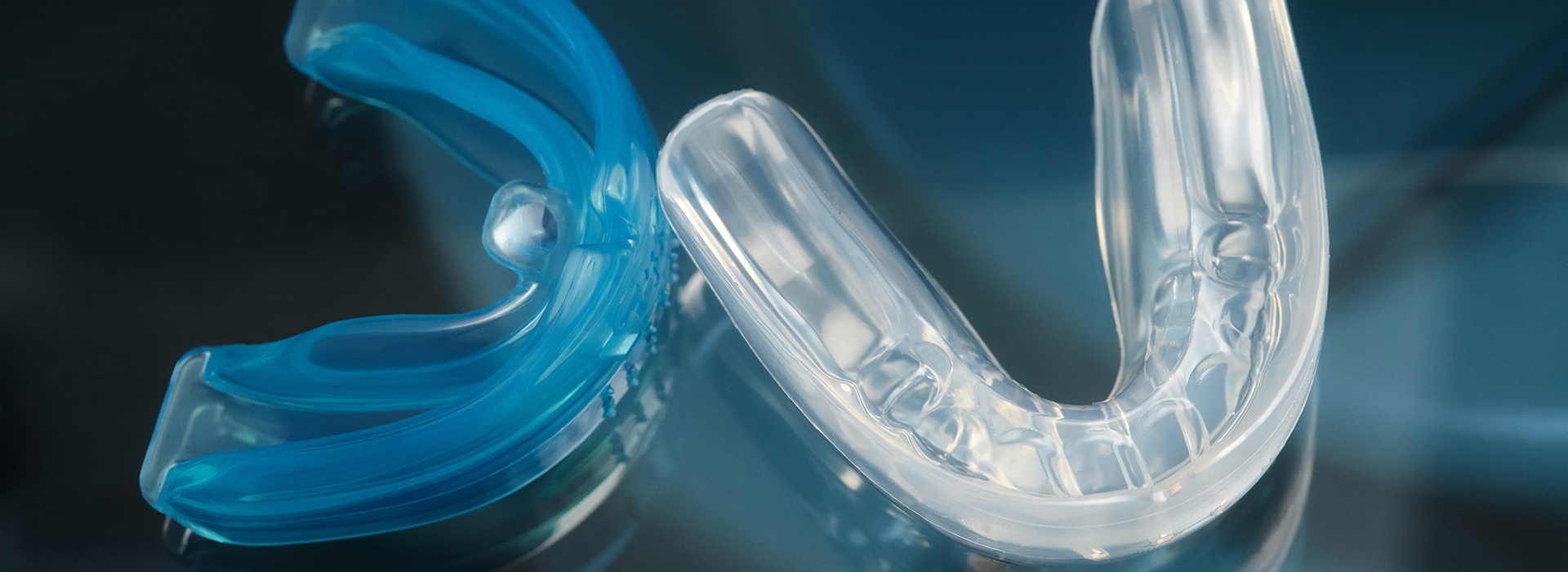 Clear plastic dental retainer with a blue-green hue, photographed against a blurred background.