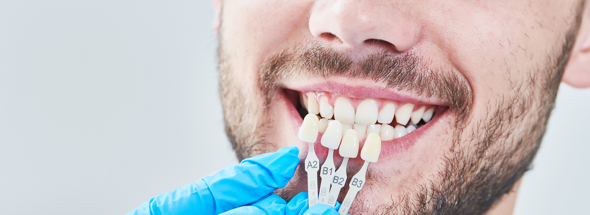 A man in a lab setting is holding a tooth with a dental implant, smiling broadly.