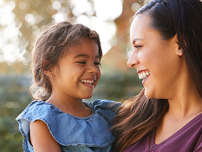 The image depicts a woman and a young child, both smiling, with the adult holding the child.