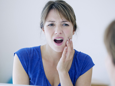 A woman with a surprised expression, touching her mouth, in front of a mirror.