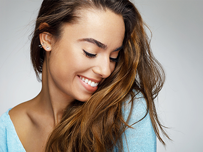 A smiling woman with long hair, wearing a light blue top, is looking to her right.