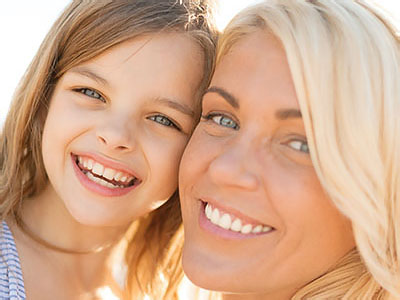 The image shows a woman and a young girl smiling at the camera, with the woman s face partially obscured by the child s.