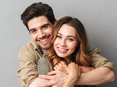 A young couple embracing and smiling, with the man wearing a casual shirt and the woman in a long-sleeve top.