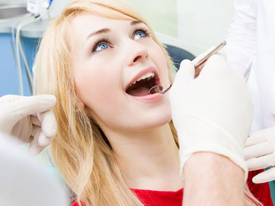 A woman in a dental chair receiving a dental procedure, with a dentist performing the treatment and a hygienist assisting.