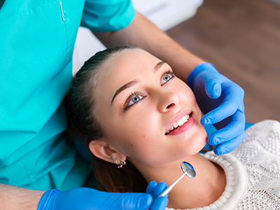 A dentist performing a dental procedure on a patient, with the patient smiling and wearing glasses.