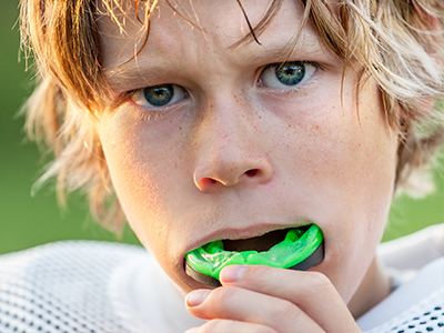 A young male athlete with blonde hair and a sports jersey, holding a green object to his mouth.