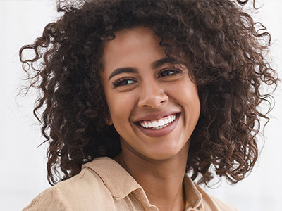 The image shows a woman with curly hair, smiling broadly and looking directly at the camera.